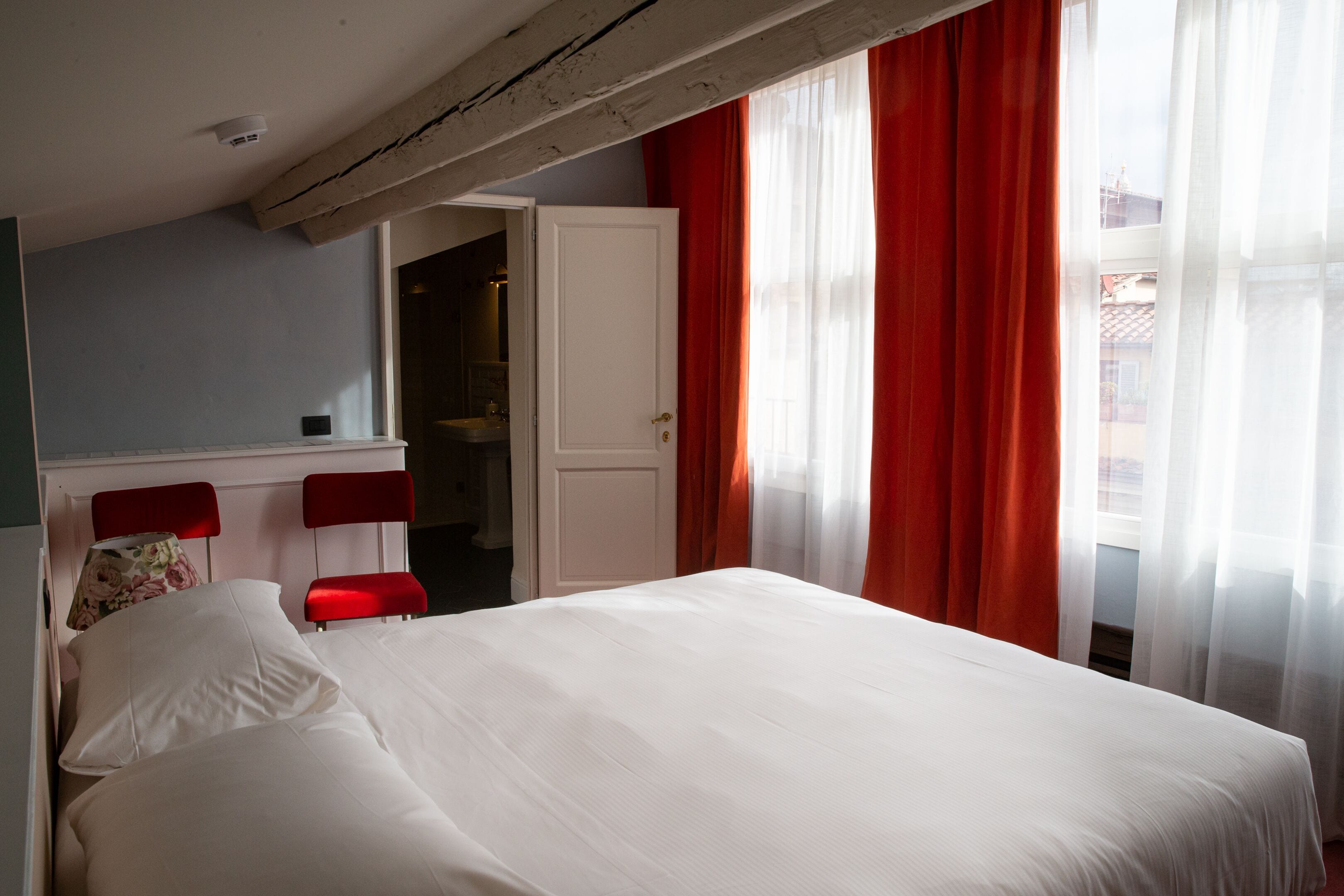 A bedroom with a bed, a red chair, a white door, and a window with red curtains.
