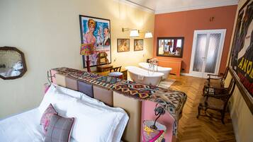 A bedroom with a bed, a bedside table, a mirror, and a bathroom with a bathtub and sink.