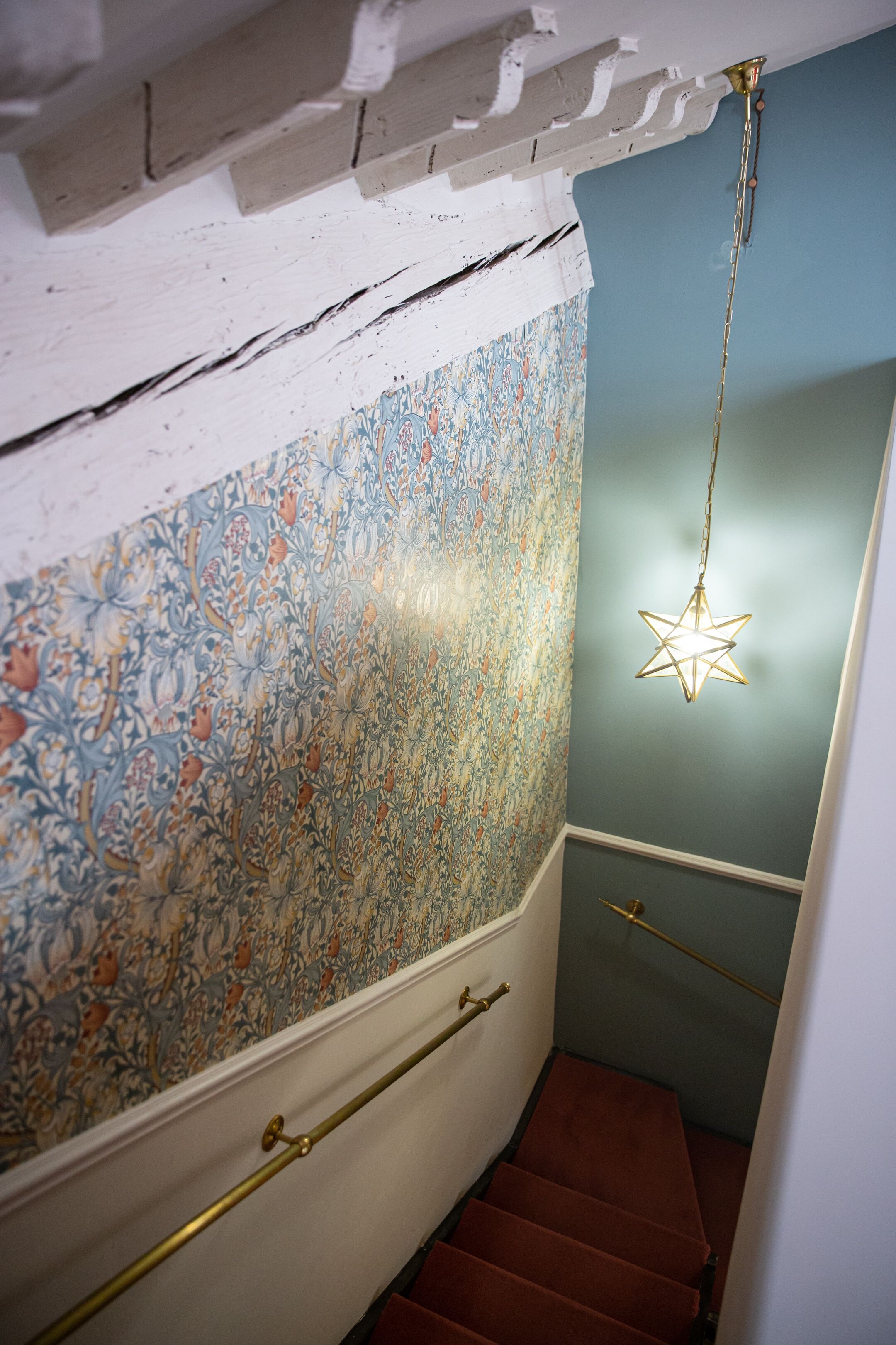 En trappa med en blommig tapet, en stjärnformad lampa och en röd matta.