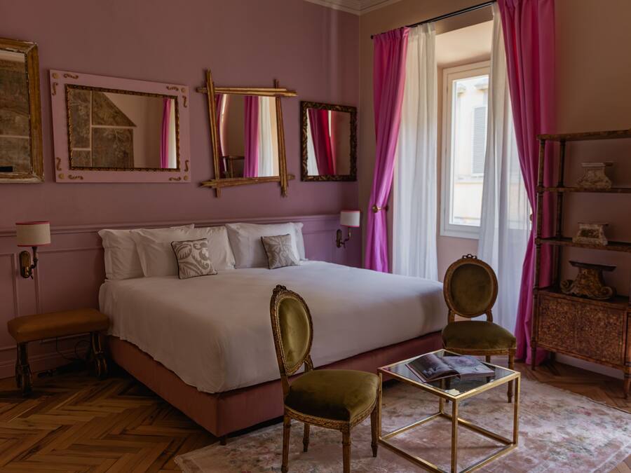 Un dormitorio con una cama grande, dos sillas, una mesita y una estantería con objetos decorativos.