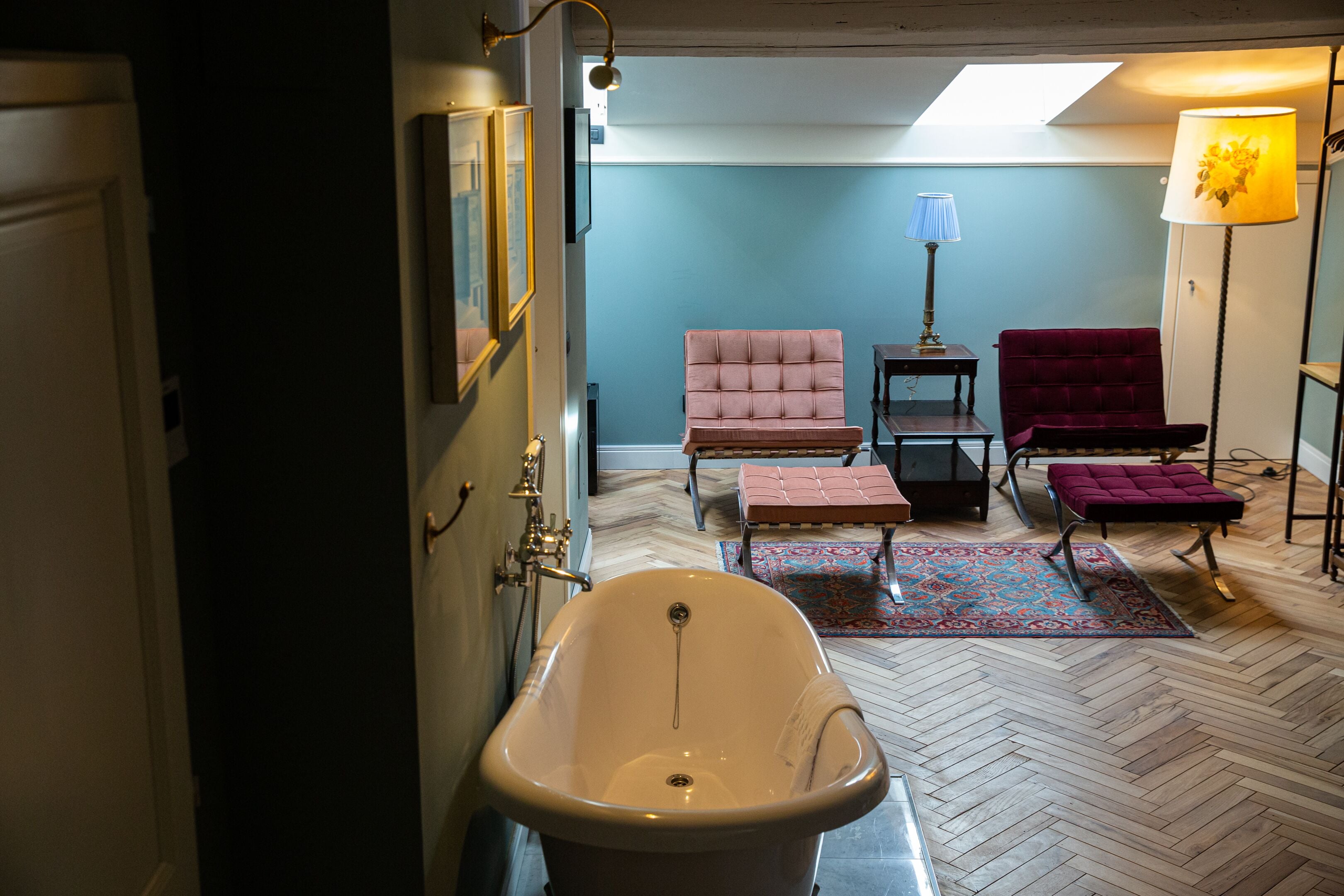 A bathroom with a freestanding bathtub, two chairs, a small table, and a floor lamp.