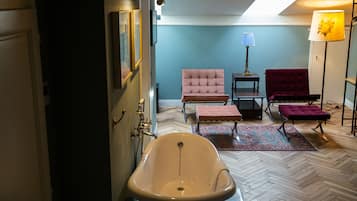 A bathroom with a freestanding bathtub, two chairs, a small table, and a floor lamp.