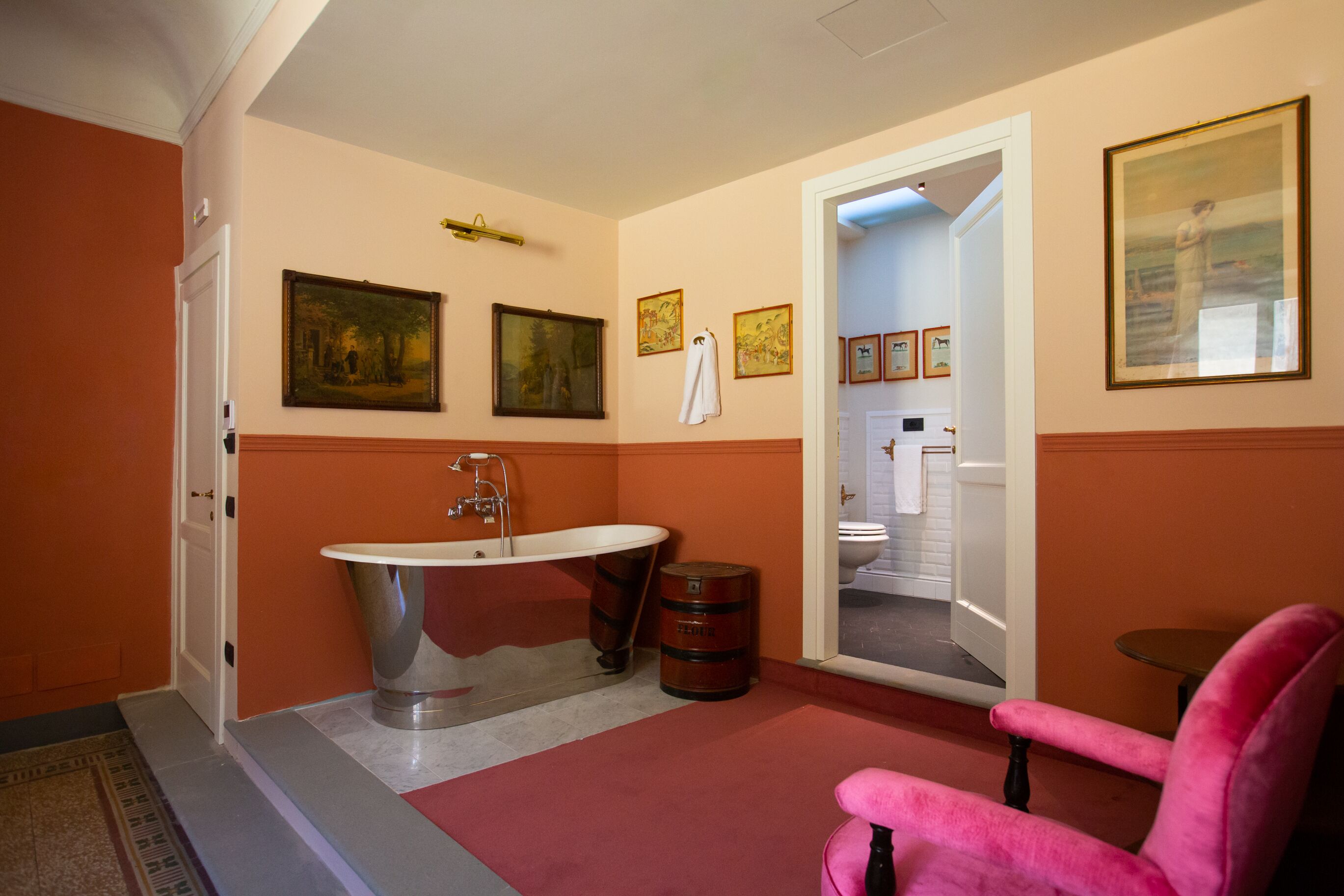 A bathroom with a bathtub, a sink, and a toilet. There are framed pictures on the wall and a pink chair in the room.