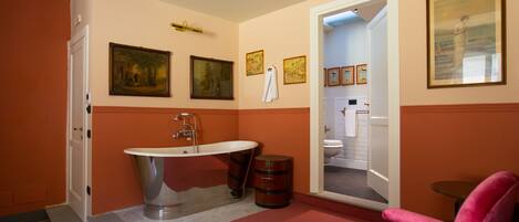 A bathroom with a bathtub, a sink, and a toilet. There are framed pictures on the wall and a pink chair in the room.