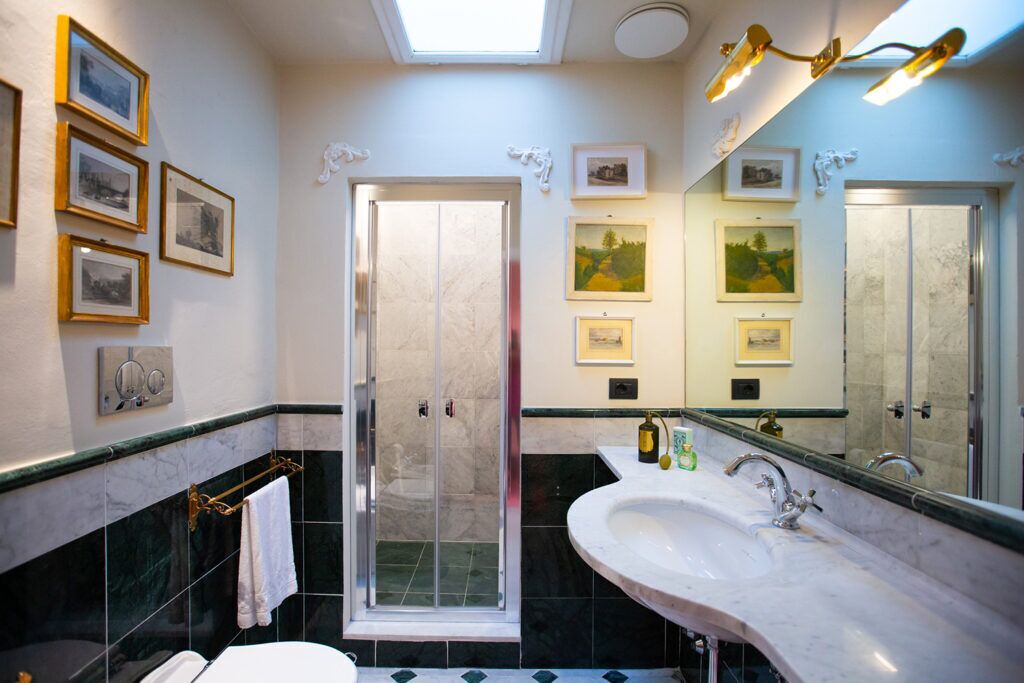 Une salle de bain avec un grand miroir, une douche, un lavabo et des tableaux encadrés accrochés au mur.