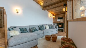 A cozy living room with a grey sofa, patterned cushions, wooden side tables, and a stone fireplace.