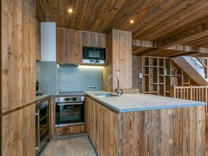 A modern kitchen with wooden cabinetry, a built-in oven, and a granite countertop. - Luxurious 5-Bedroom Chalet Apartment with Panoramic Mountain View, Wi-Fi, and Garage (Val-d'Isère)