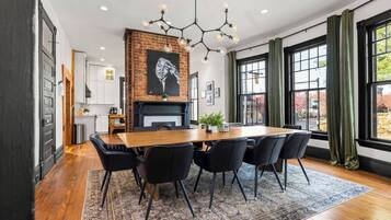 A modern dining area with a brick fireplace, a chandelier, and a large window with curtains.