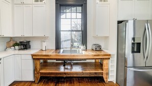 Una cucina con mobili bianchi, un piano di lavoro in legno, un frigorifero in acciaio inossidabile e una finestra con vista all'esterno.
