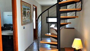 En spiralopsats med trætrin og sorte gelændere, der fører op til en etage ovenpå. En lampe står på et bord til højre.