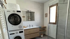 Un baño moderno con lavadora, lavamanos, espejo y cabina de ducha de vidrio.