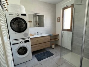 A modern bathroom with a washing machine, a sink, a mirror, and a glass shower enclosure.