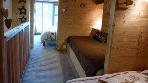 A cozy cabin bedroom with a wooden interior, a bed with a brown blanket, and a window with a view of trees. - Cozy duplex for 5 with balcony and WIFI in Arc 1800 (Les Arcs 1800)