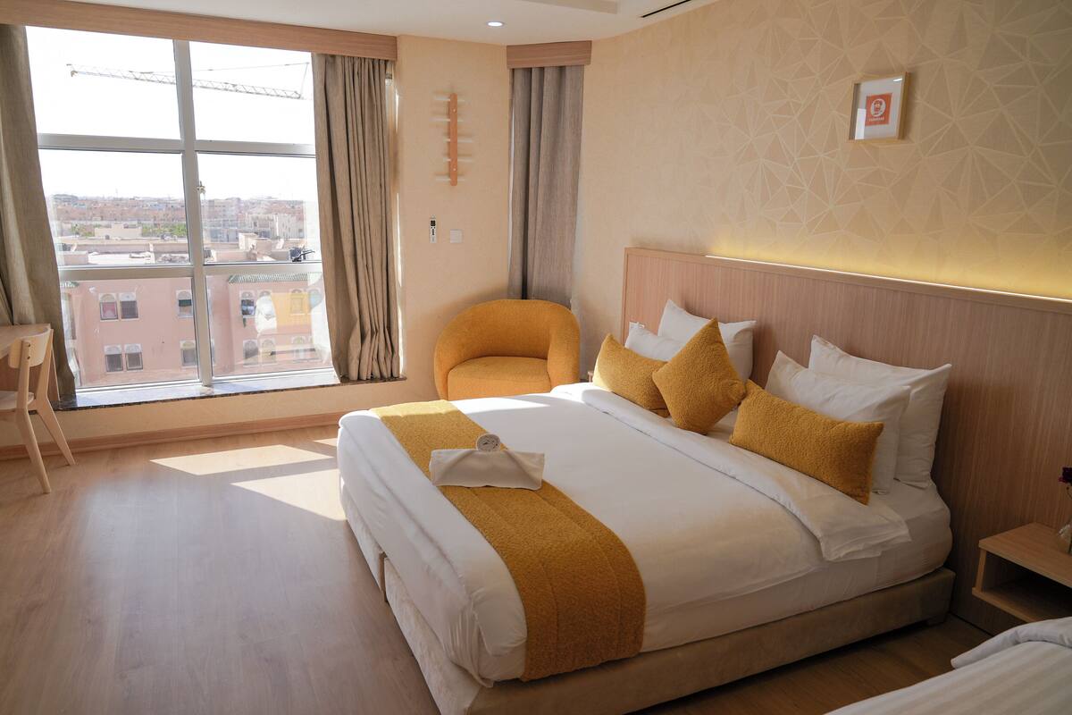 Habitación de hotel con una cama grande, una silla y vistas a la ciudad a través del ventanal.
