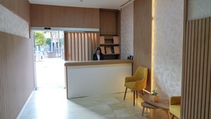 A reception area with a wooden reception desk, two yellow chairs, and a small table with a plant.