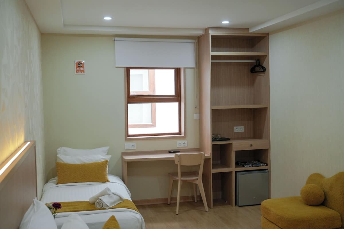 Habitación de hotel con cama, escritorio, silla, refrigerador pequeño y armario.