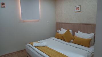 A neatly made bed with white and mustard bedding, a wooden headboard, and a geometric patterned wall.