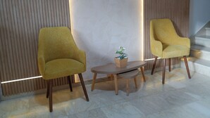 A reception area with two yellow armchairs, a small wooden table with a potted plant, and a staircase in the background.