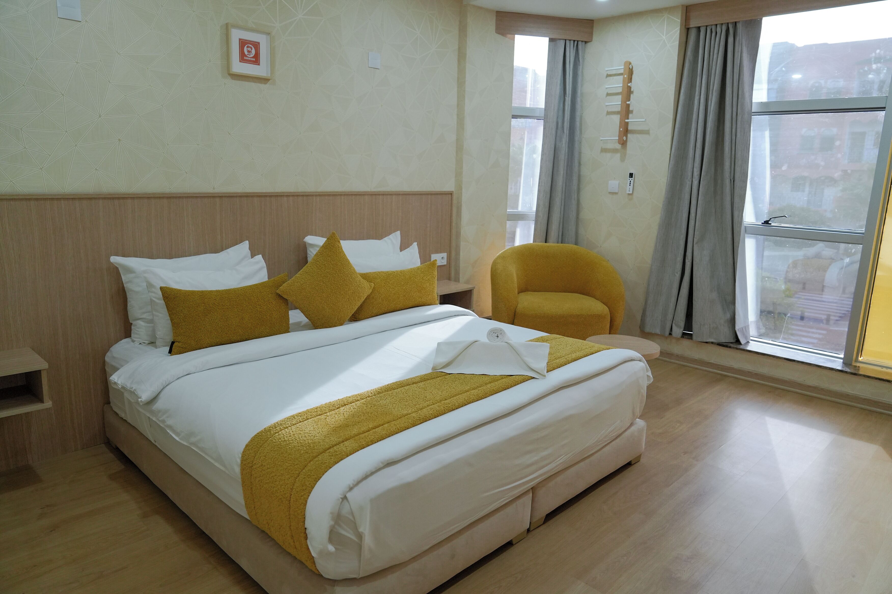 A hotel room with a large bed, a yellow armchair, and a window with curtains.