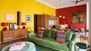 Un salón vibrante con un sofá verde, un aparador de madera y un comedor con pared roja y ventilador de techo.