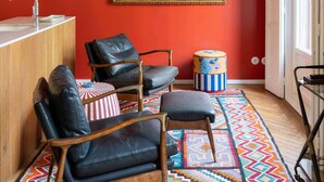 Una habitación con pared roja, un cuadro, un escritorio de madera, dos sillones de cuero, un tapiz colorido y una ventana.