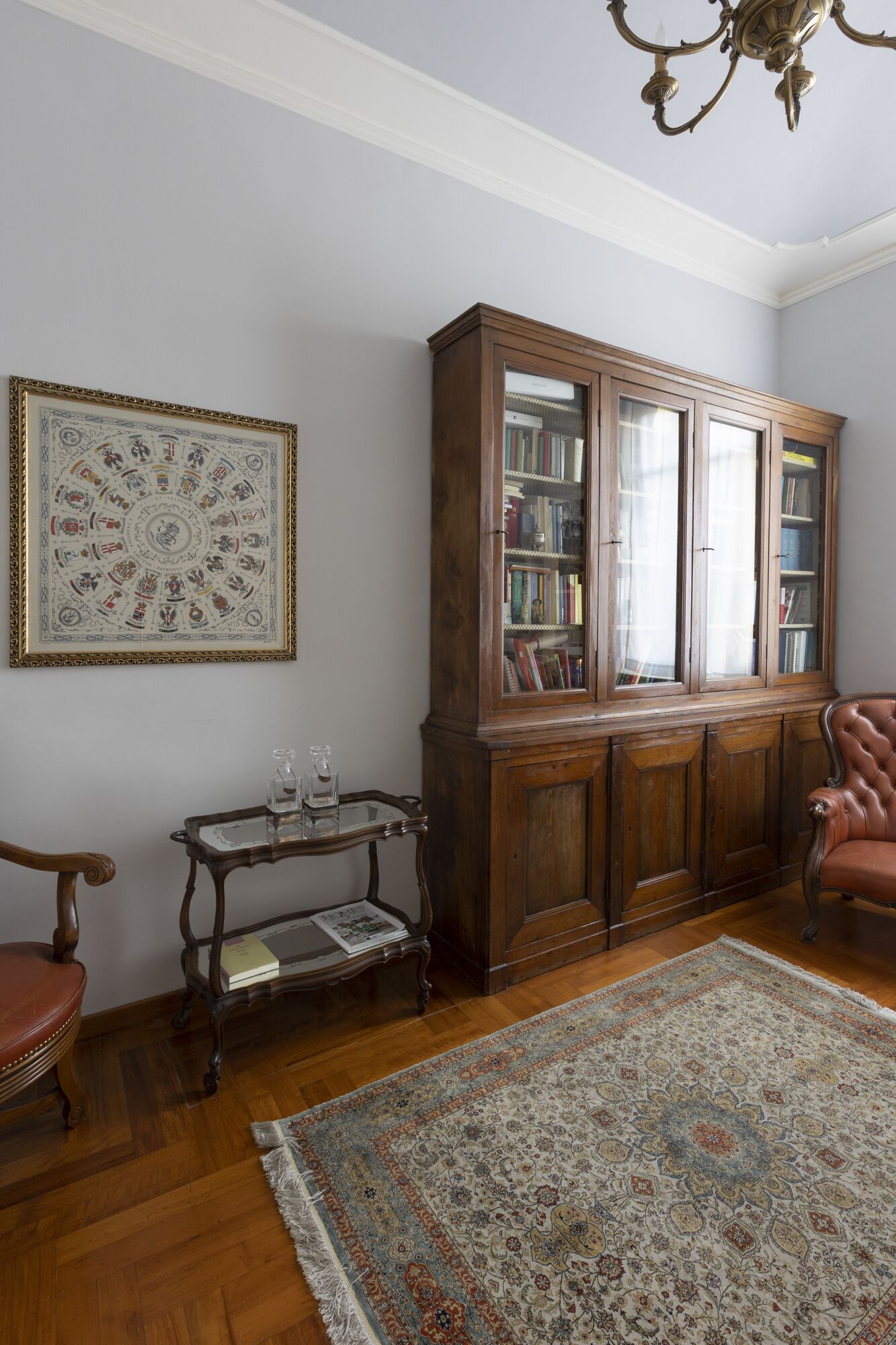 A room with a wooden cabinet, a glass-top table, a patterned rug, and a chair.