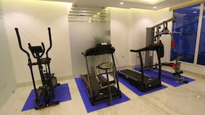 Une salle de sport à domicile équipée de trois appareils d’exercice placés sur des tapis bleus, d’un tapis de course et d’un banc de musculation.