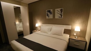 Une chambre d’hôtel comprenant un lit, deux tables de chevet avec lampes, une armoire et deux œuvres d’art accrochées au mur.
