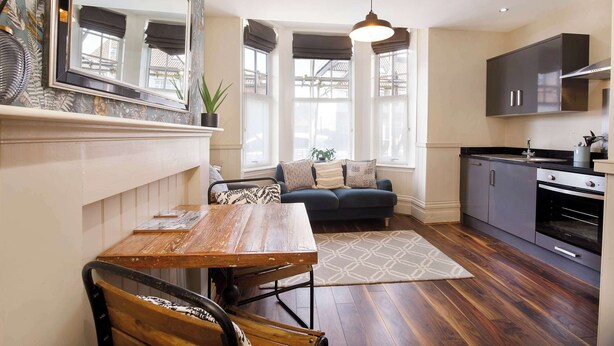 A compact living space with a dining table, a sofa, a kitchen area, and large windows with blinds.