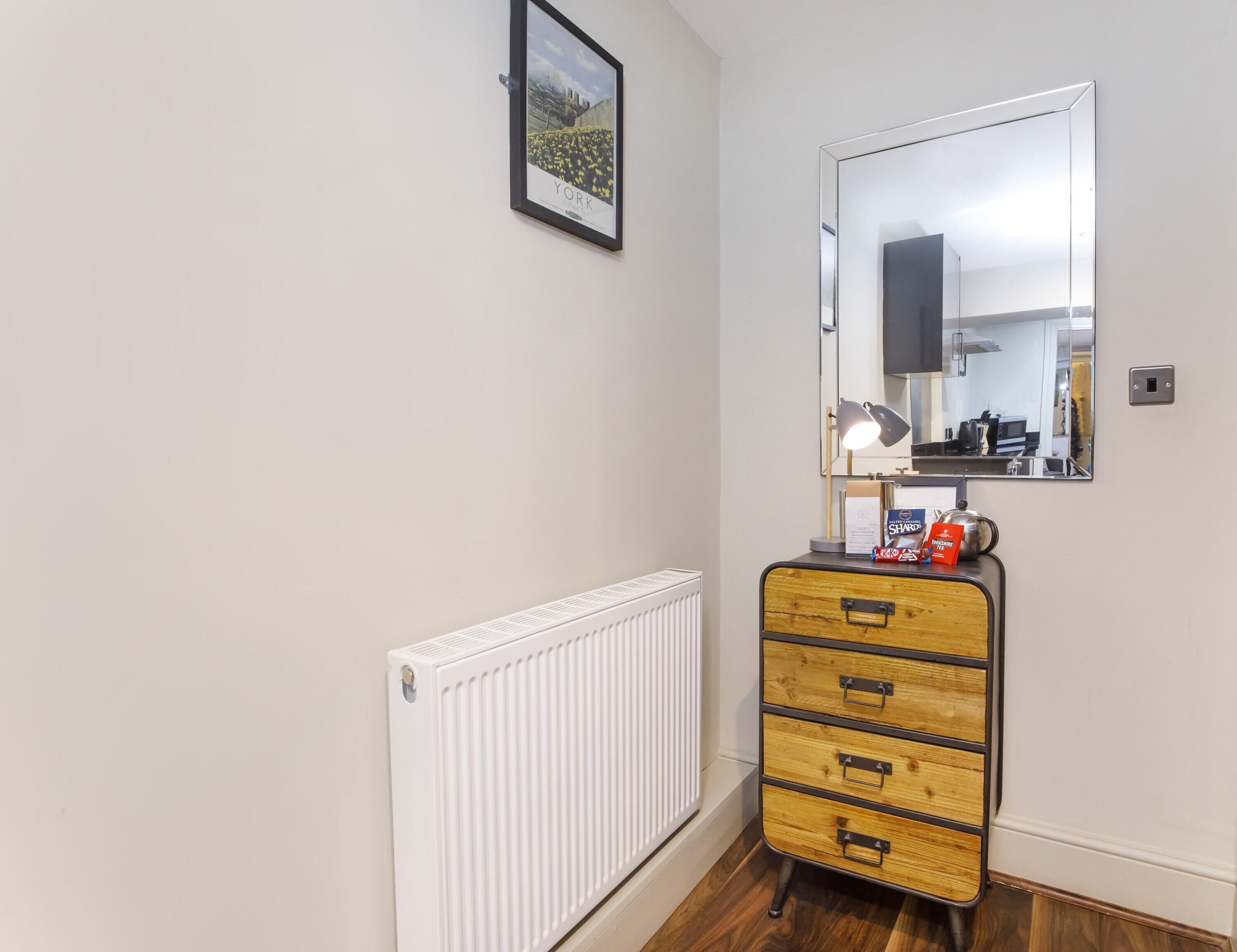 A small room with a radiator, a wooden dresser with drawers, a mirror, and a framed picture on the wall.