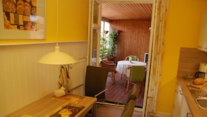 A dining area with a table, chairs, a lamp, and a view into a dining room with a table and chairs.