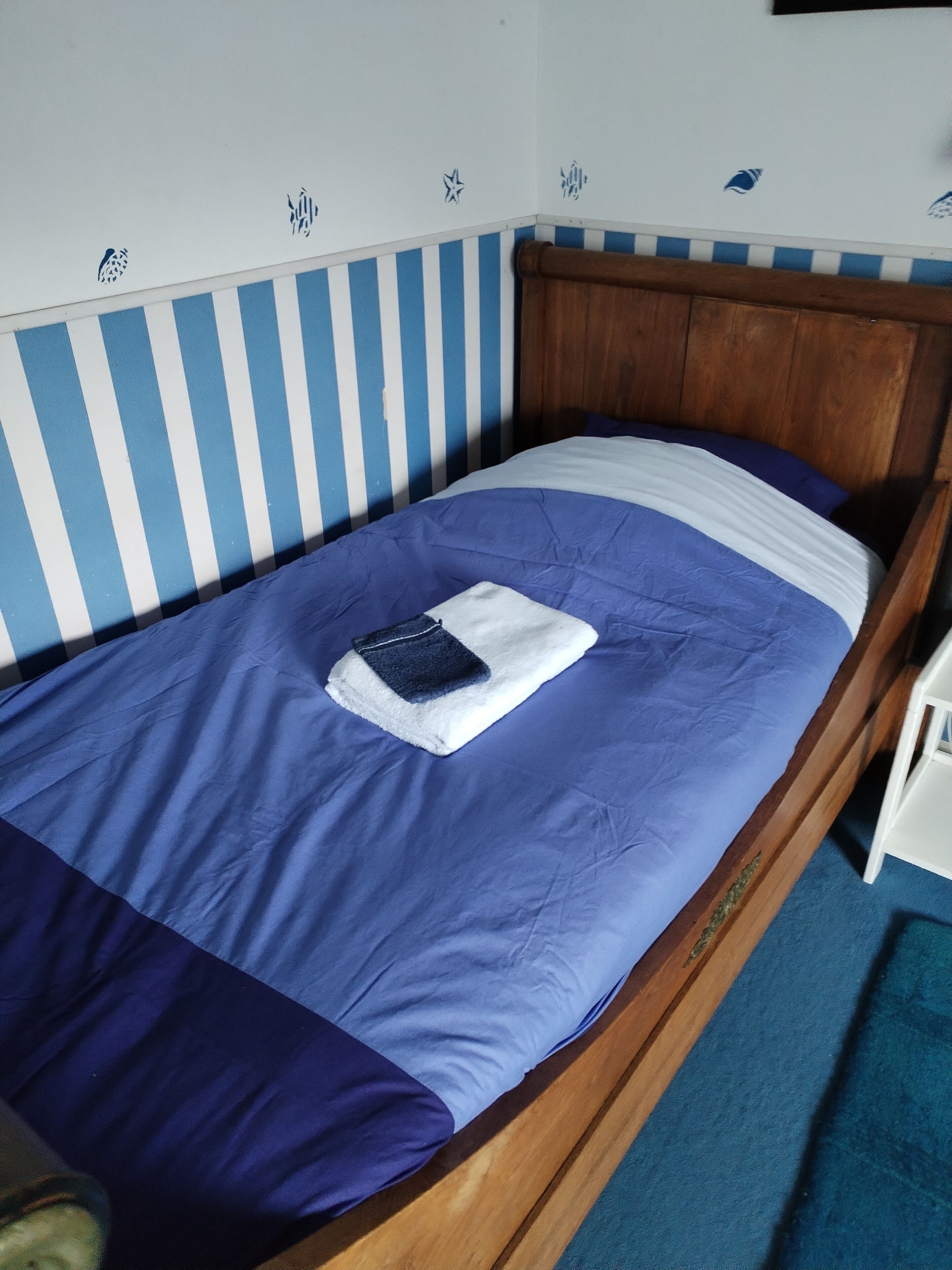 Una cama individual con cabecera azul y blanca a rayas, cabecera de madera y colcha azul y blanca.