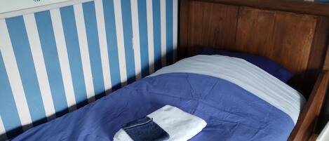 Una cama individual con cabecera azul y blanca a rayas, cabecera de madera y colcha azul y blanca.