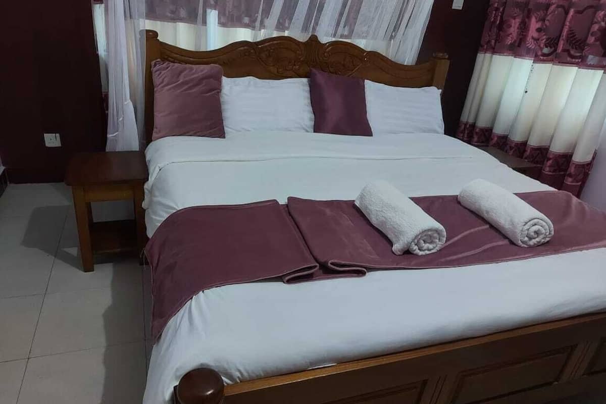 A neatly made bed with a wooden headboard, white and purple bedding, and two rolled towels on the bed.
