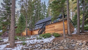 A log cabin with a wooden exterior, a stone retaining wall, and a staircase leading to the upper level. - Modern cabin retreat! Cozy, scenic, and serene! (Carnelian Bay)