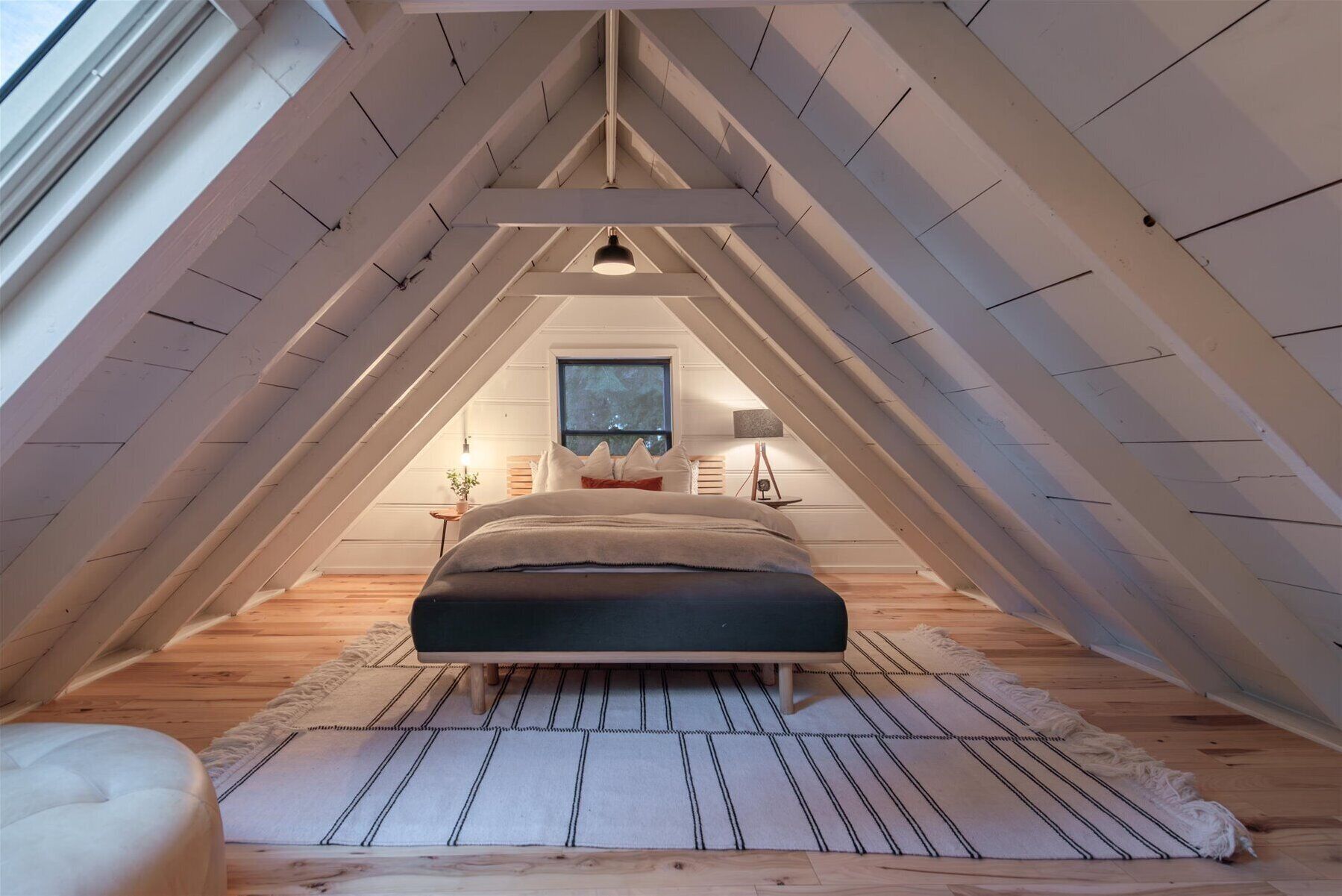 Accogliente camera mansardata con un letto, un comodino, una lampada e vista sul cielo notturno attraverso una finestra.