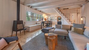 A cozy living room with a fireplace, a staircase, and large windows offering a view of the outdoors. - Modern cabin retreat! Cozy, scenic, and serene! (Carnelian Bay)