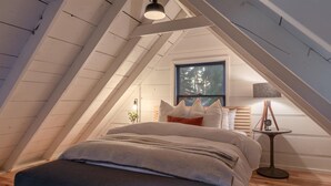 A cozy attic bedroom with a sloped ceiling, a bed with a striped blanket, a bedside table with a lamp, and a window with a view of trees. - Modern cabin retreat! Cozy, scenic, and serene! (Carnelian Bay)