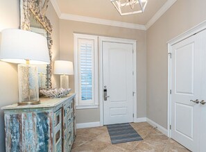 A hallway with a white door, a mirror with a decorative frame, and two lamps on a rustic dresser.