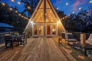 Une terrasse en bois avec une table à manger et des chaises, un barbecue et un coin salon avec des coussins.