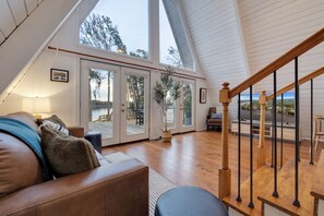 A spacious living area with a high ceiling, a wooden staircase, and a view of a lake.