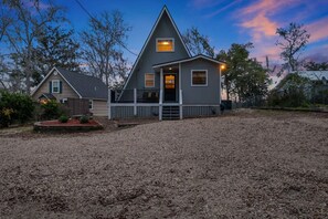 A two-story house with a front porch, a small deck, and a gravel driveway.