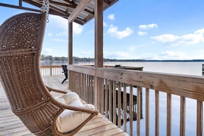 Una terraza de madera con una silla mecedora de mimbre y vistas a un lago tranquilo.