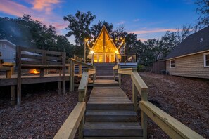 A wooden deck leading to a building with a triangular roof, surrounded by trees and a clear sky. - Talquin Triangle: Lakefront - A frame - Fire Pit (Quincy)