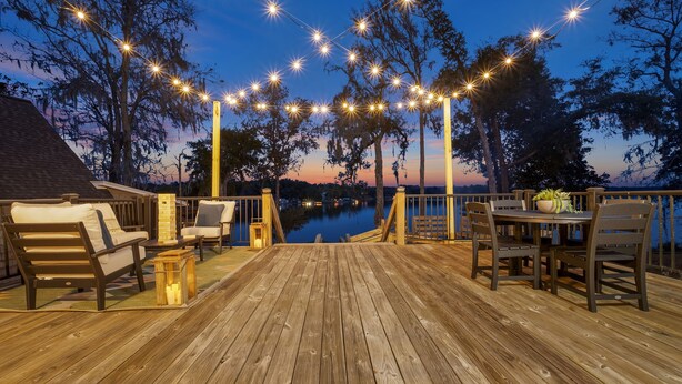 Une terrasse en bois, dotée de meubles d’extérieur, de guirlandes lumineuses et offrant une vue sur l’eau.