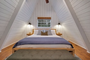 Un dormitorio con techo inclinado, una cama con cabecera de madera, dos lámparas de noche y una ventana.