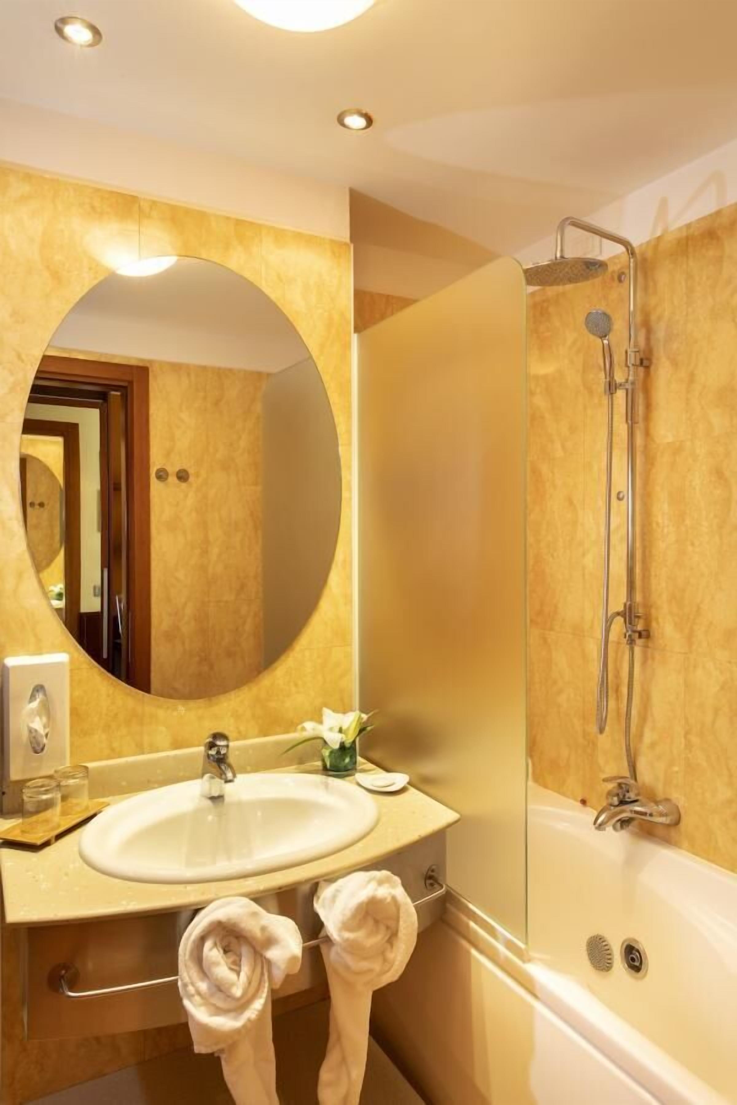 A bathroom with a round mirror, a sink, and a shower.