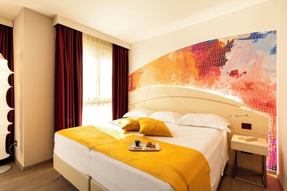 Ein Hotelzimmer mit Bett, Nachttisch, digitaler Uhr und einem Kunstwerk an der Wand.