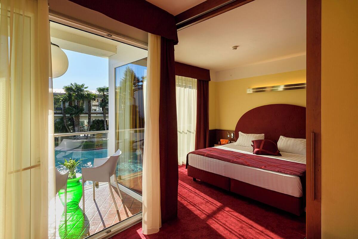 Ein Hotelzimmer mit Bett, einem Balkon mit Glasdoor und Blick auf Palmen.