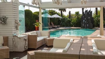 Un área de piscina interior con mobiliario de mimbre y un muro de cristal.